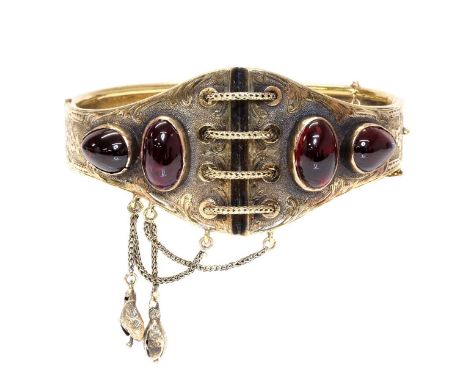 A Victorian gold garnet set hinged bangle, c.1860,of graduated corset form. A centrepiece with a laced corset or bodice, with