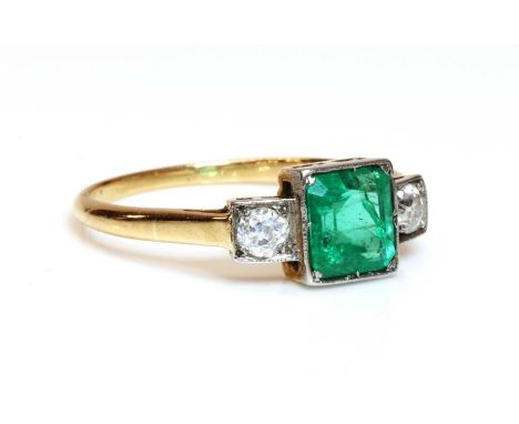 A three stone emerald and diamond ring,with a square cut emerald, spitch set to a white setting edge to a yellow collet. An o