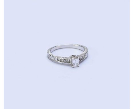 A single stone diamond ring, the rectangular cut diamond claw set in white metal to diamond set shoulders, the white metal sh