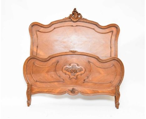 An early-mid 20th century French, Louis XV style, walnut veneered double bed, carved with rocaille work and a floral panel on