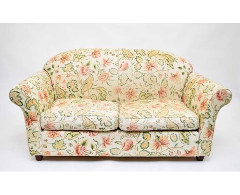 A Wesley Barrell two-seater sofa, covered with pastel coloured floral fabric, with an arched back and scroll arms, with fire 