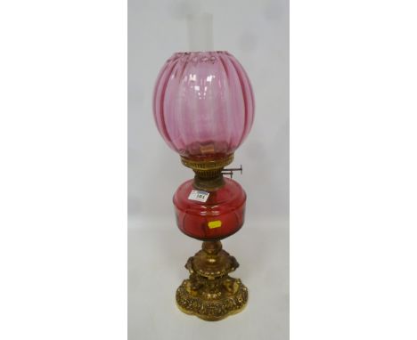 19th/ early 20th Century oil lamp with cranberry glass well and shade, with ornate gilded metal base  Condition Report Click 