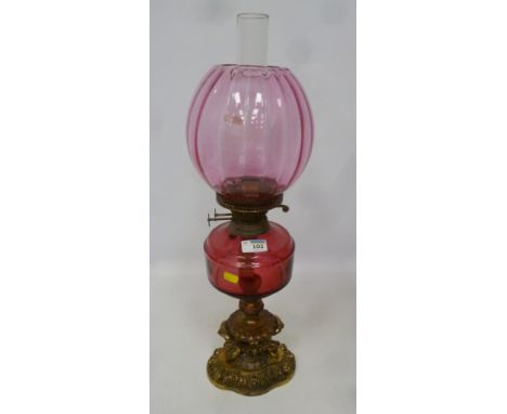19th/ early 20th Century oil lamp with cranberry glass well and shade, with ornate gilded metal base (matching previous lot) 