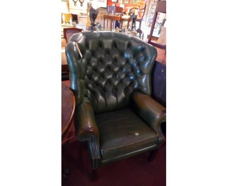 A green leather wing back armchair with button back upholstery and raised on reeded square legs 