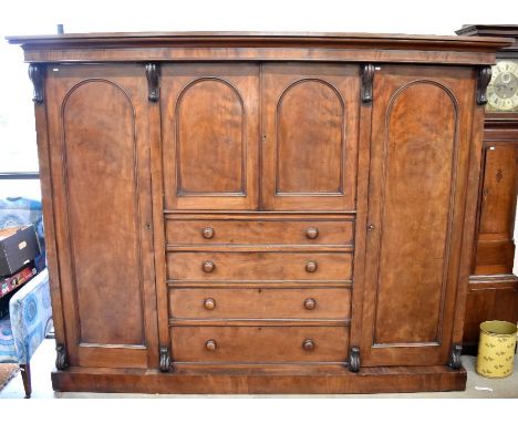A large Victorian mahogany compactum wardrobe with arched panelled doors enclosing slides and hanging space and four central 