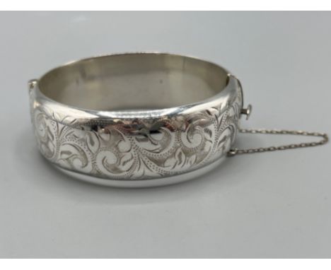 Ladies silver hinge broad patterned bangle with safety chain. 32.4g