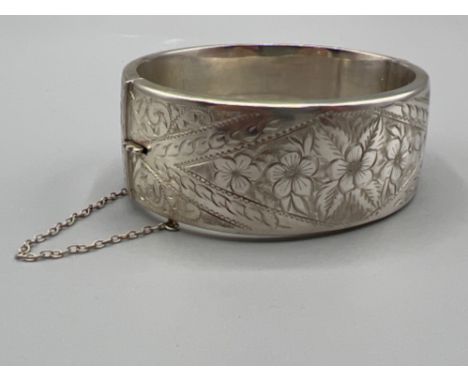 Ladies sterling silver broad patterned bangle with safety chain. 38.8g