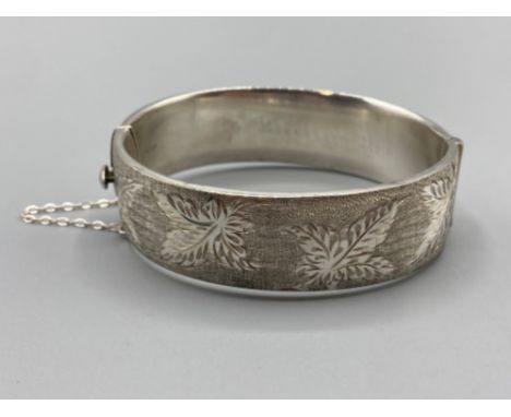 Ladies silver hinged broad bangle, with leaf pattern on the front complete with safety chain, 46.4g