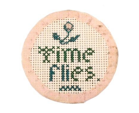 A watch case sampler, of circular form worked in green cross stitch on Bristol card with a flower over ‘Time flies’, within a