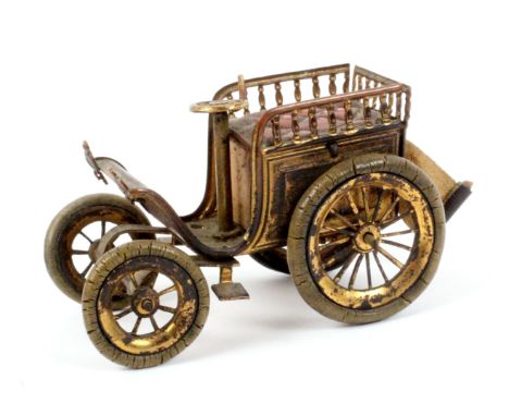 A scarce brass novelty tape measure in the form of a veteran car, the wheels with rubber tyres, red patterned seat within bal