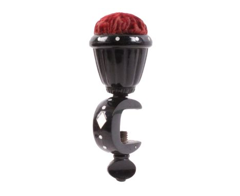 A black horn sewing clamp, embellished with mother of pearl dots and a diamond, the curved frame below a vase form pin cushio