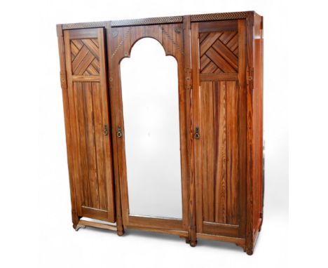 A Victorian aesthetic movement Arts and Crafts pitch pine triple wardrobe with a central mirrored door and fitted interior, i