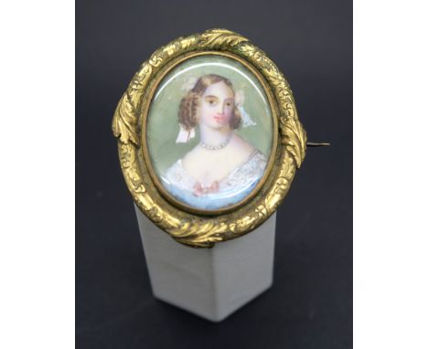 A XIX Century Painted Miniature Oval Brooch, depicting a lady with bows in hair and pearl necklace, with applied engraved lea