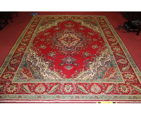 A large Iranian red ground woollen rug, the stylised central field within trailing tramline borders, 325 x 260cmCondition rep
