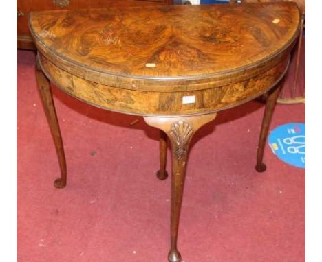 A 1930s figured walnut and crossbanded demi-lune fold over baize lined card table, raised on shell capped cabriole supports, 