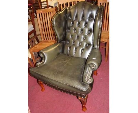 A contemporary green leather button back upholstered and further brass studded wing back scroll armchair, raised on acanthus 