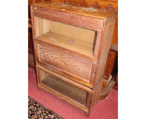 A 1930s limed oak three-tier stacking book case, having two glazed hinged panel doors, and one further timber panelled door, 