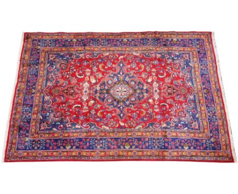 A red ground Persian Mashad carpet, the central blue medallion upon a trailing ground enclosed by spandrels and borders, 299c