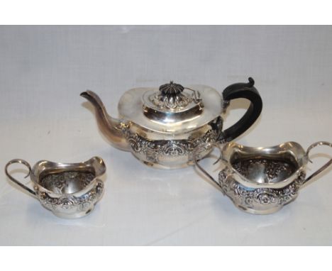 An Edward VII silver three-piece tea set comprising an oval tea pot with raised scroll decoration and ebonised handle togethe