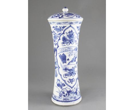 A tall Chinese blue and white waisted cylindrical jar and cover, Kangxi period, painted with shaped panels of ribbon tied obj
