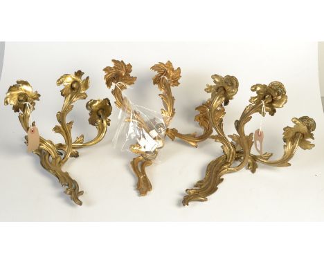 A pair of gilt metal rococo three branch wall light fittings and one other similar fitting.