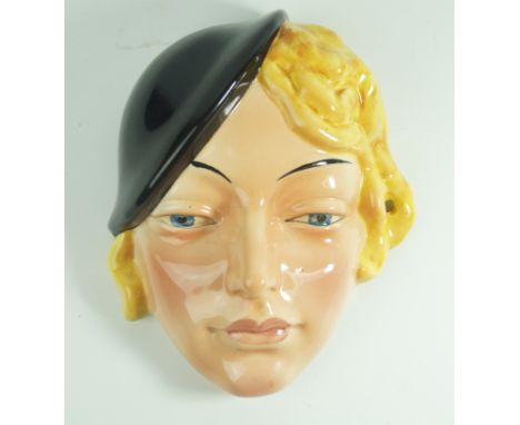 A Beswick Art Deco ceramic wall maskModelled in the form of a girl with blonde hair wearing a black hat, printed factory mark