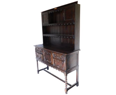 A 1920's oak dresser, the plate rack having one short shelf flanked by a pair of cupboards, over a long shelf, above a cupboa