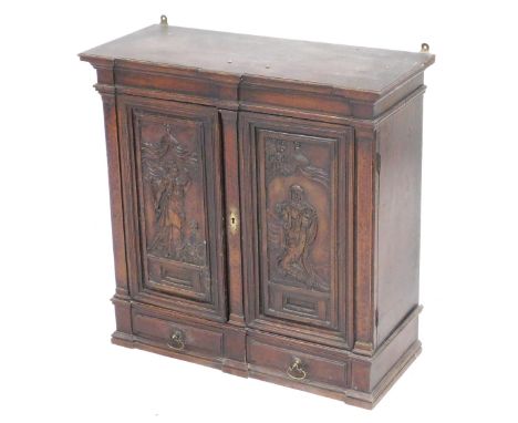 A late 17thC Continental walnut sacristy cabinet, the pediment top over a pair of panelled doors carved with religious figure