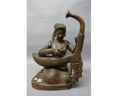 A Burmese wood figure of a musician, 20th century, carved as a seated young woman playing the harp, 53cm. high.