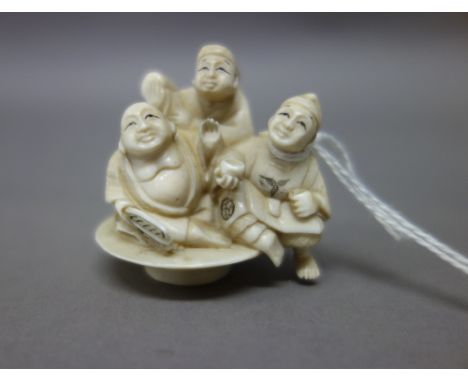 A Japanese ivory netsuke, early 20th century, carved with three figures including Hotei and Daikoku, signed, 4.5cm. high; als