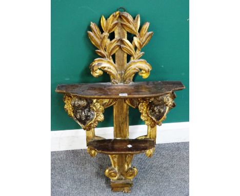 An 18th century and later North European giltwood two tier wall shelf, with winged cherub mounts amongst acanthus sprays, 55c