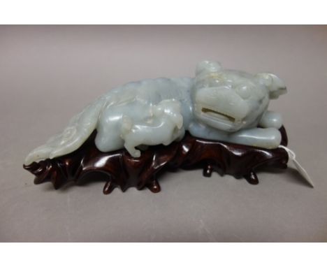 A Chinese greyish-celadon jade lion group, 19th century, carved with a recumbent lion with incised mane and long tail, its he