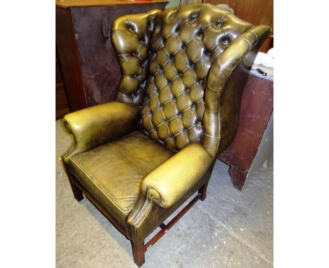 A 20th century mahogany framed wingback armchair with green leather button back upholstery on square block supports.  Dis