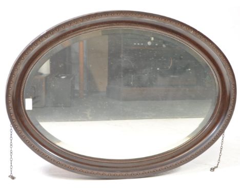 A vintage early 20th century oval wall hanging mirror. The mirror with wooden carved frame and bevelled edged glass. Featurin