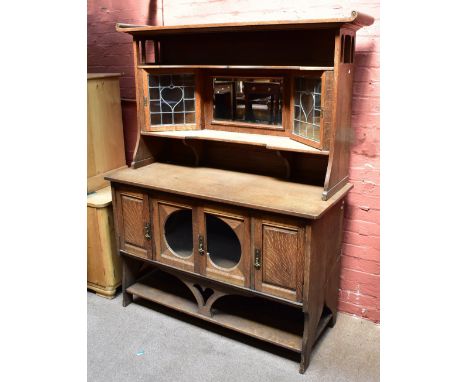 An Arts and Crafts oak sideboard, the back section with fixed shelf above central bevelled mirror plate flanked by two lead g