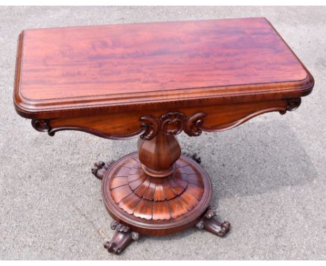 An early Victorian mahogany fold over swivel top games table with carved decoration to the skirt, raised on a octagonal balus