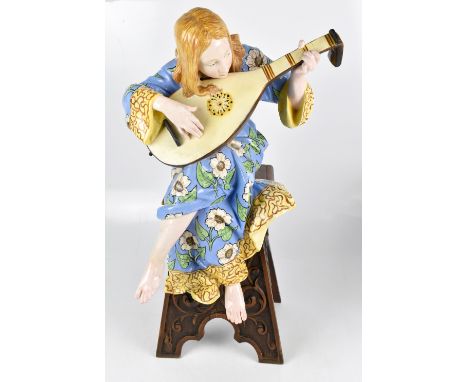 An early 20th century Italian faience ware figure representing a maiden wearing a floral blue and mustard coloured gown playi