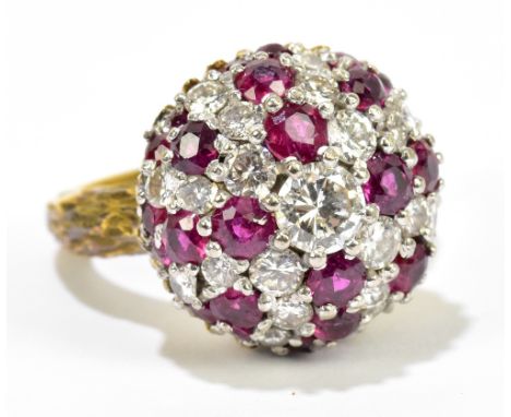 A textured yellow metal diamond and ruby domed ring, the central round brilliant cut stone weighing approx. 0.25cts, within a