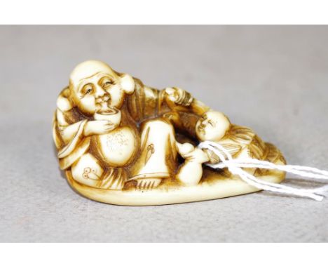 Antique Japanese carved ivory netsuke seated man with child. Export of this item would be subject to CITES approval. Length 5