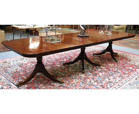 A Regency Style Mahogany Three Pillar Dining Table, with three additional leaves, on outswept supports capped with brass paw 