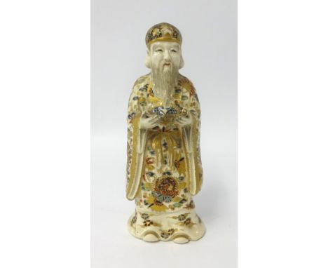 A Chinese porcelain figure of a man with long beard, gilt decorated cloak and hat reading a scripture, indistinct marks to ba