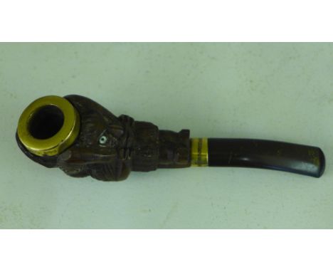 A carved Maori wooden pipe bowl carved as a prow head with grimacing face, facing backwards with mother of pearl eyes carved 