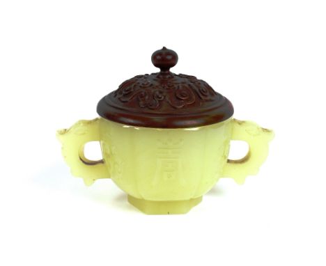 A jade two handled cup, decorated symbols with angular handles complete with carved hardwood cover, 12cm long x 8cm high over