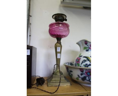 A brass oil lamp with cranberry coloured glass reservoir.
