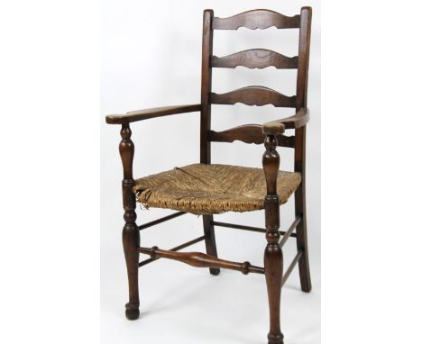 A 20thC ash and elm ladder backed carver chair, with rush seat, turned front supports and cylindrical front with a baluster c