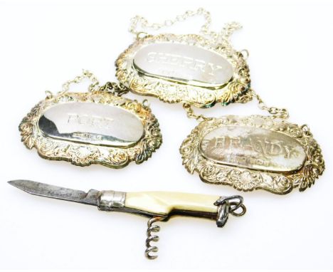 An early 20thC novelty bottle shaped pen knife and corkscrew, with hook top, 6cm high, and three various silver spirit labels