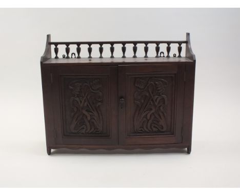 An Art Nouveau carved walnut two door wall cabinet, with spindle gallery shelf above two indented cabinet doors carved with l