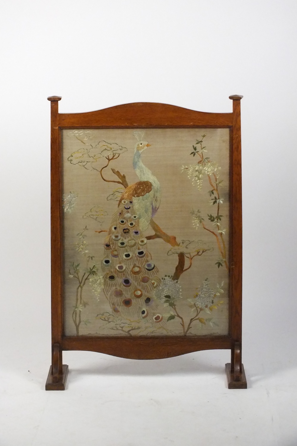 An Arts and Crafts oak fire screen with silk tapestry work panel of a peacock on sledge feet, 68c