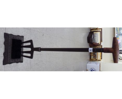 A modern cast iron boot scraper, fashioned as a garden fork with a wooden handle       CA