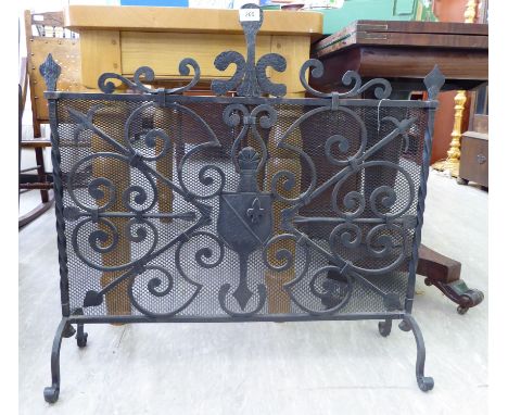An early 20thC wrought iron firescreen with a mesh back, twin C-scrolled and arrowhead ornament, raised on splayed legs  30''